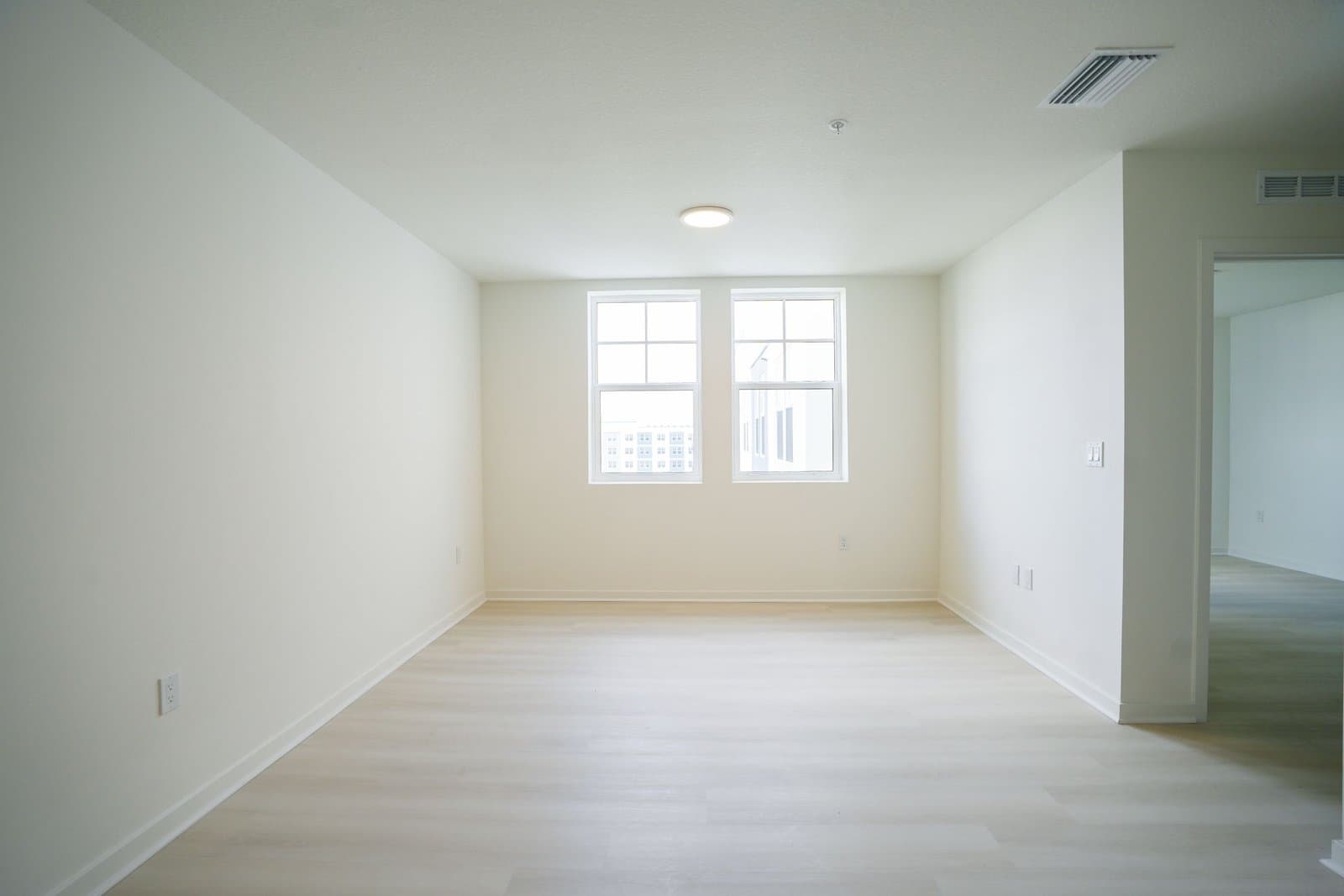 Bright empty room with white walls, a light wood floor and two windows