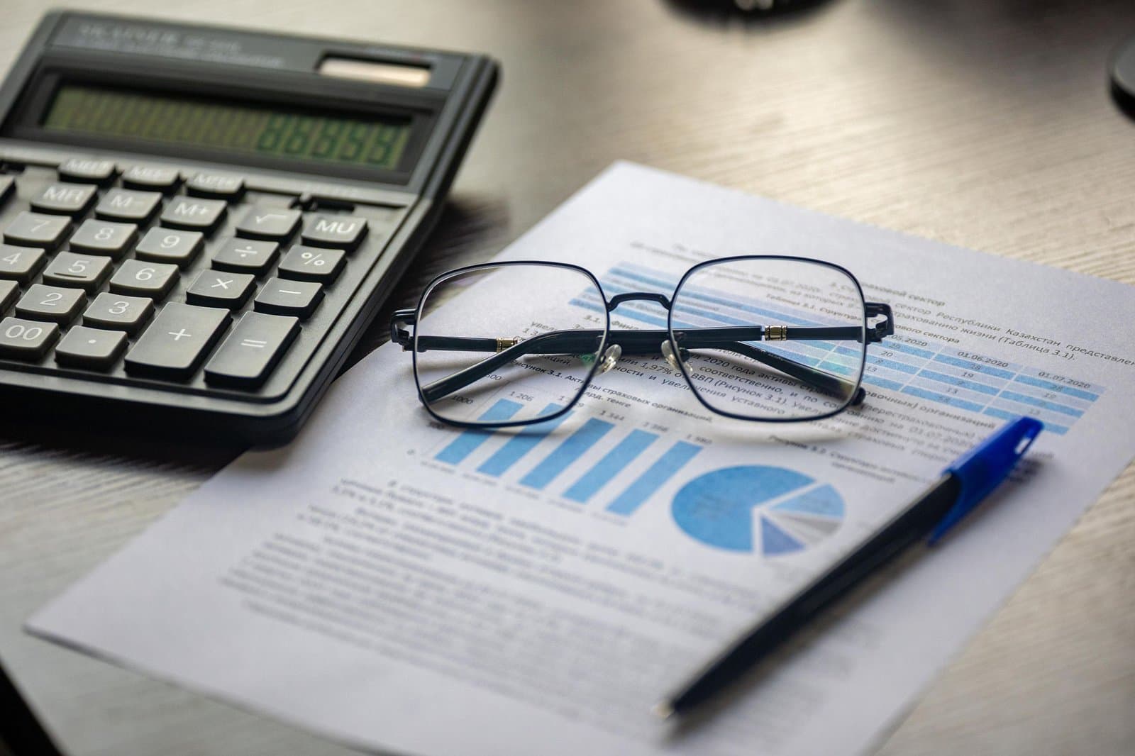 Printed report with bar and pie charts, reading glasses, a pen and a calculator on a desk